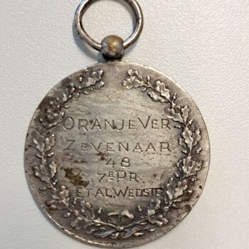 Medaille van verzilverd metaal  met gegraveerde tekst 7de prijs van de etalagewedstrijd uitgereikt door de Oranjevereniging Zevenaar in 1848