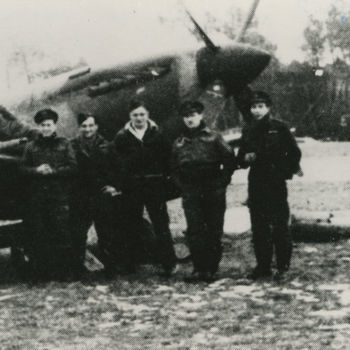 Groeps foto van groep zes mannen in R.A.F. uniform voor Supermarine Spitfire. Tekst achterop: "Spitfire 322 Sqn. op vliegveld Woensdrecht. In 't midden met witte trui F/Sgt Cramm". Tekst er onder: "Flight-sergeant Cramm van 322 Sqdn. Hij wordt op 30-3-1945 met zijn Spitfire bij Almen neergechoten en komt om".