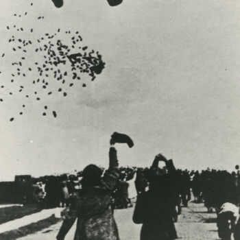 Foto van een Avro Lancaster die voedsel afwerpt, vanaf de grond toegejuicht door Nederlandse burgers. Tekst achterop: "29-4-1945. Voedseldropping voor Lancaster (15 Sqn) nabij Rotterdam".