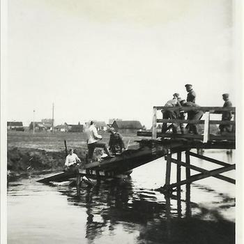 Mannen, o.a. soldaten, op deels ingestorte houten brug boven rivier