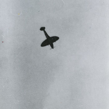 Foto van Spitfire in flauwe duikvlucht, van onder af gefotografeerd. Tekst: "Spitfire tijdens beschieting van weg-verkeer in hetr najaar van 1944".