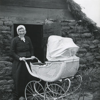 Drentse vrouw met kinderwagen voor een plaggenhut in openluchtmuseum Schoonoord, 1954