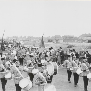 Op de hoek van de Teisterbantlaan Nieuwe Tielseweg marcheert tijdens het Oogstfruitcorso een muziekkorps. Op de achtergrond de Gemeentelijke Mavo