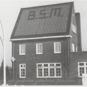 Woning of kantoorpand met letters B.S.M. verwerkt in het dak, autobus aan de linkerzijde. Uithangbord Shell op voorgrond. B.S.M. is de Betuwse Streekvervoer Maatschappij, operend tussen 1966-1971, daarna overgenomen door de Zuid-Ooster.