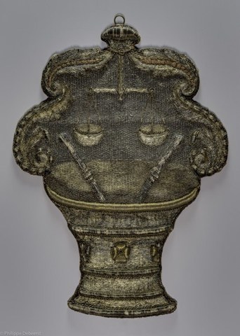 Wapenschild van het ambacht van de Gentse Kruideniers, kaaskopers en kaarsgieters, met voorstelling van een vijzel met twee stampers waarboven een weegschaal